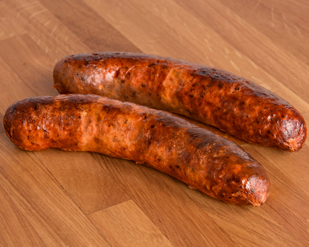 Two cooked sausages with a glossy, seasoned surface resting on a wooden surface.