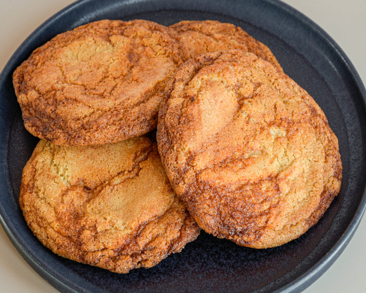 Four golden-brown gochuijang caramel cookies piled on a dark gray ceramic plate, shown in a close-up shot.