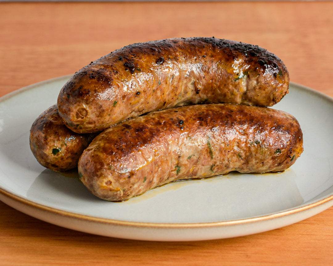 Three grilled sausages with charred marks, served on a light gray ceramic plate with a gold rim on a wooden table.
