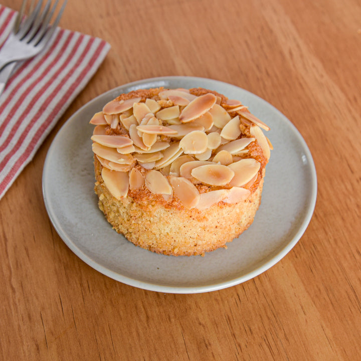Small brown butter almond torte topped with slivered almonds on a blue plate